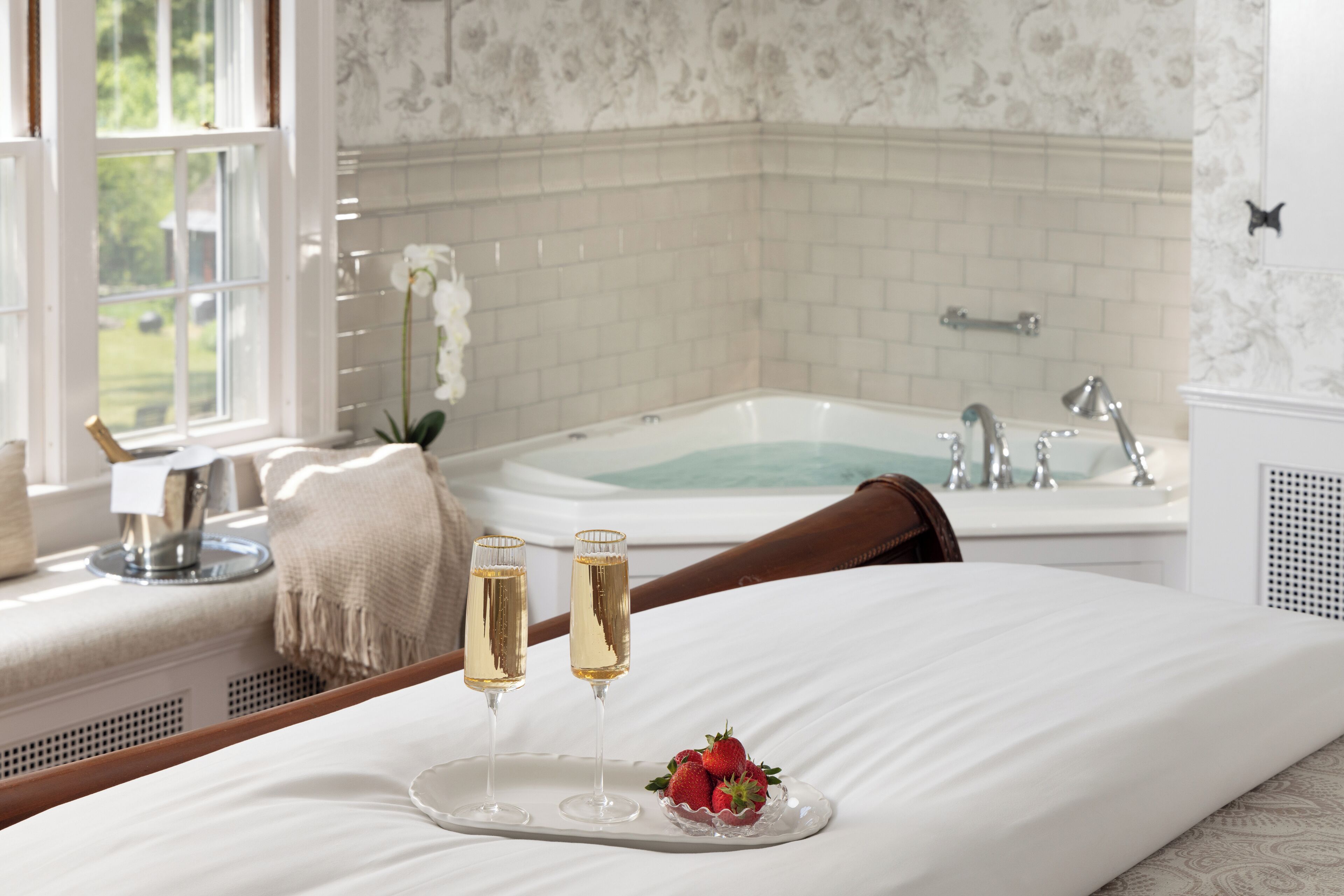 Ett hotellrum med en säng, ett badkar och två glas champagne på ett brickbord.