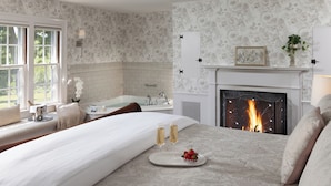 Une chambre dotée d’un grand lit, d’une cheminée, d’une baignoire et d’une fenêtre donnant sur un paysage verdoyant.