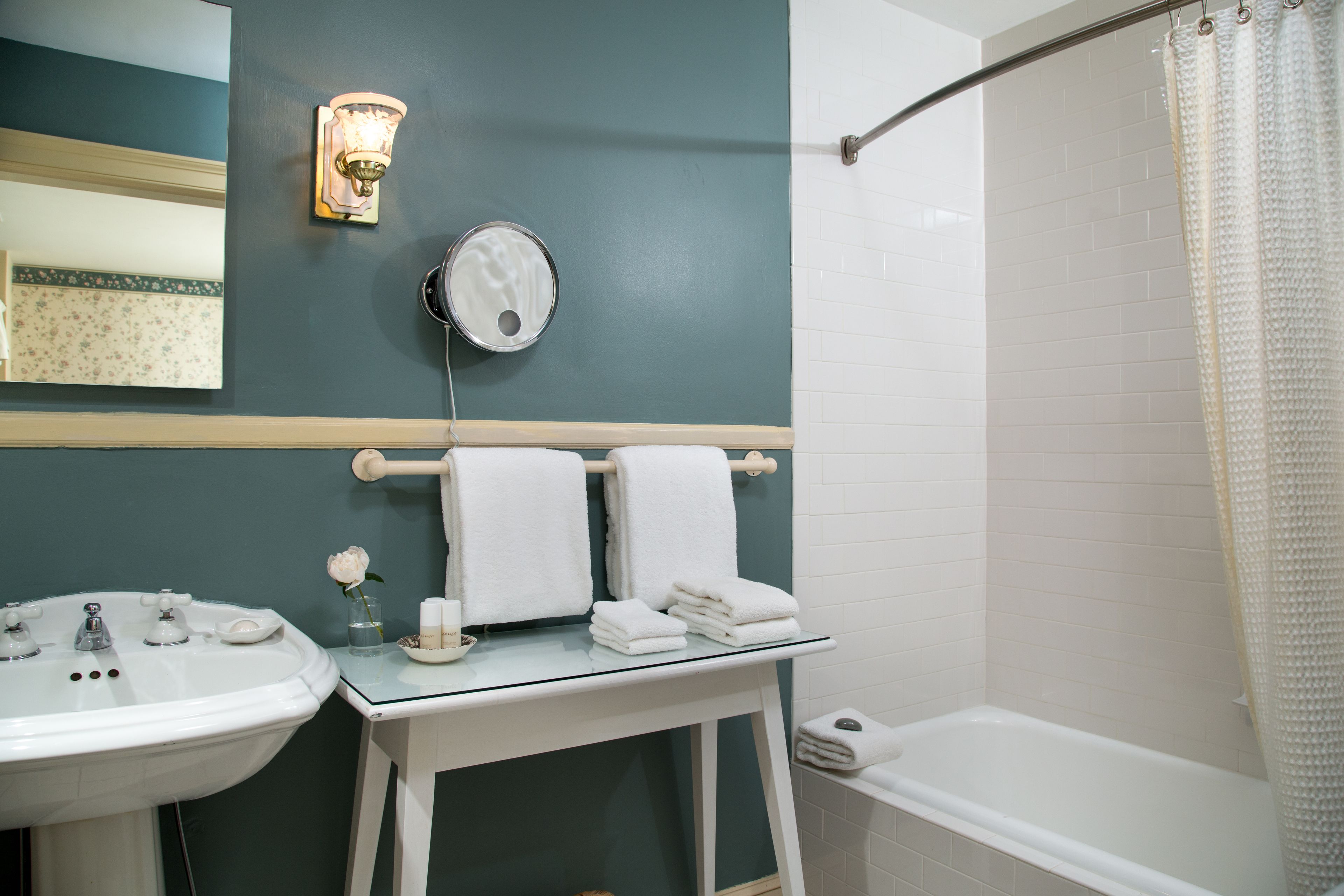 A bathroom with a sink, mirror, and a glass-topped vanity with towels.