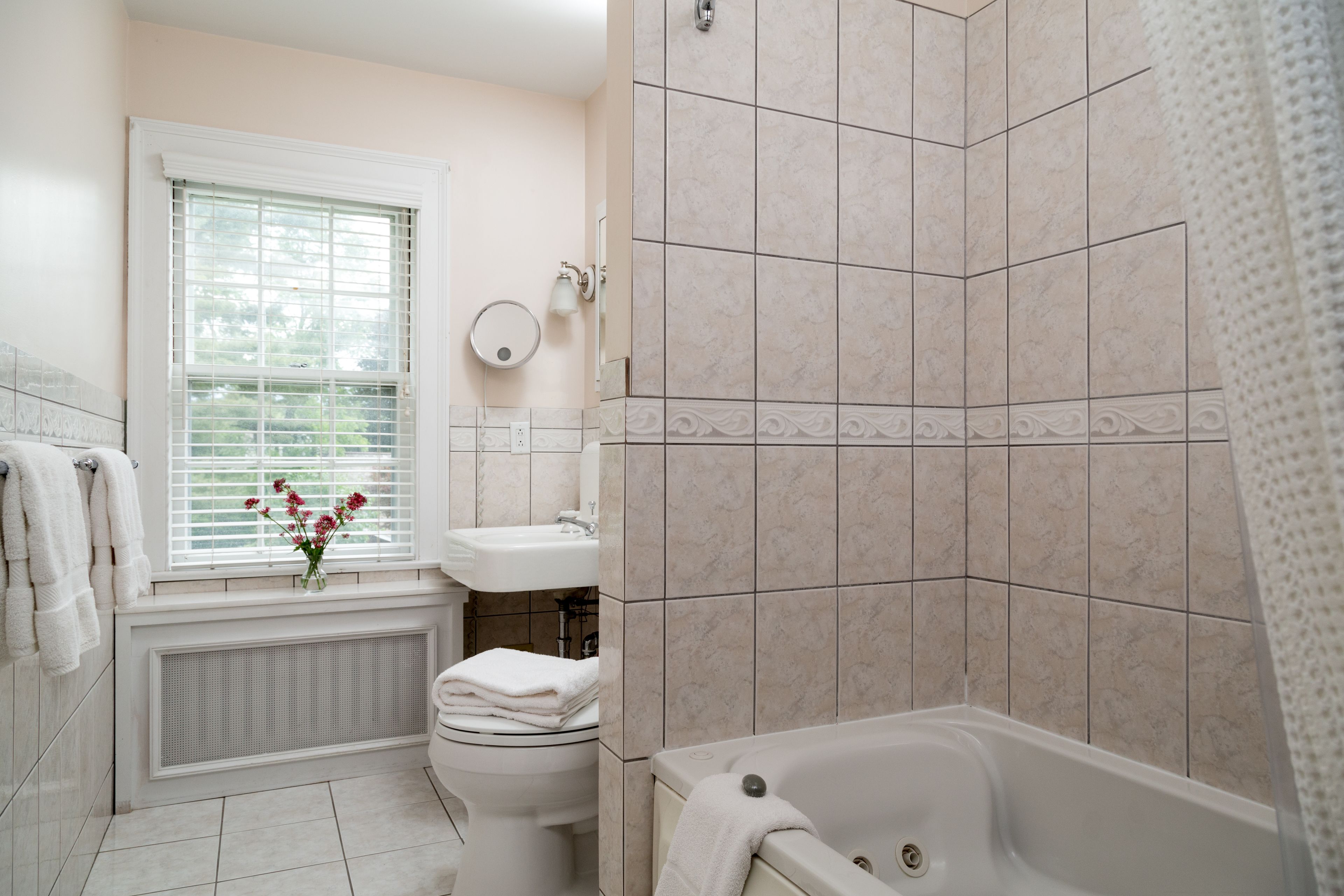 A bathroom with a toilet, sink, bathtub, and window with blinds.