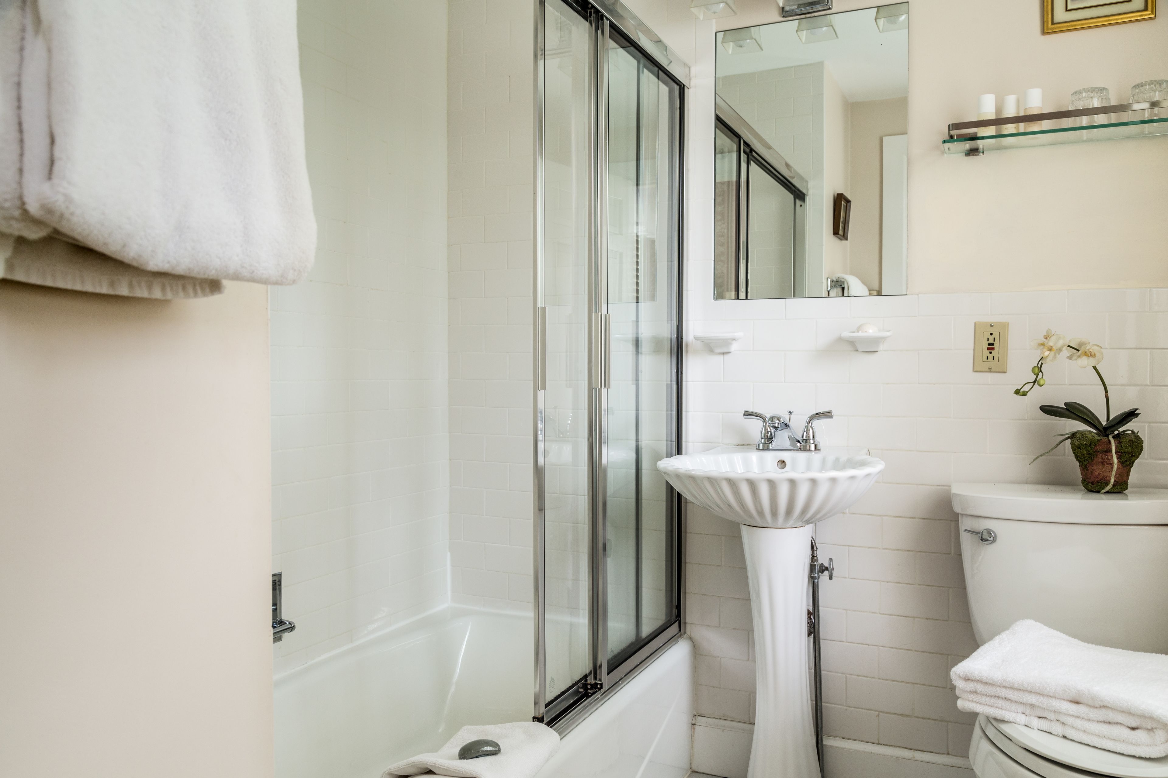 Een badkamer met een douchecabine van glas, een witte wastafel en een toilet.