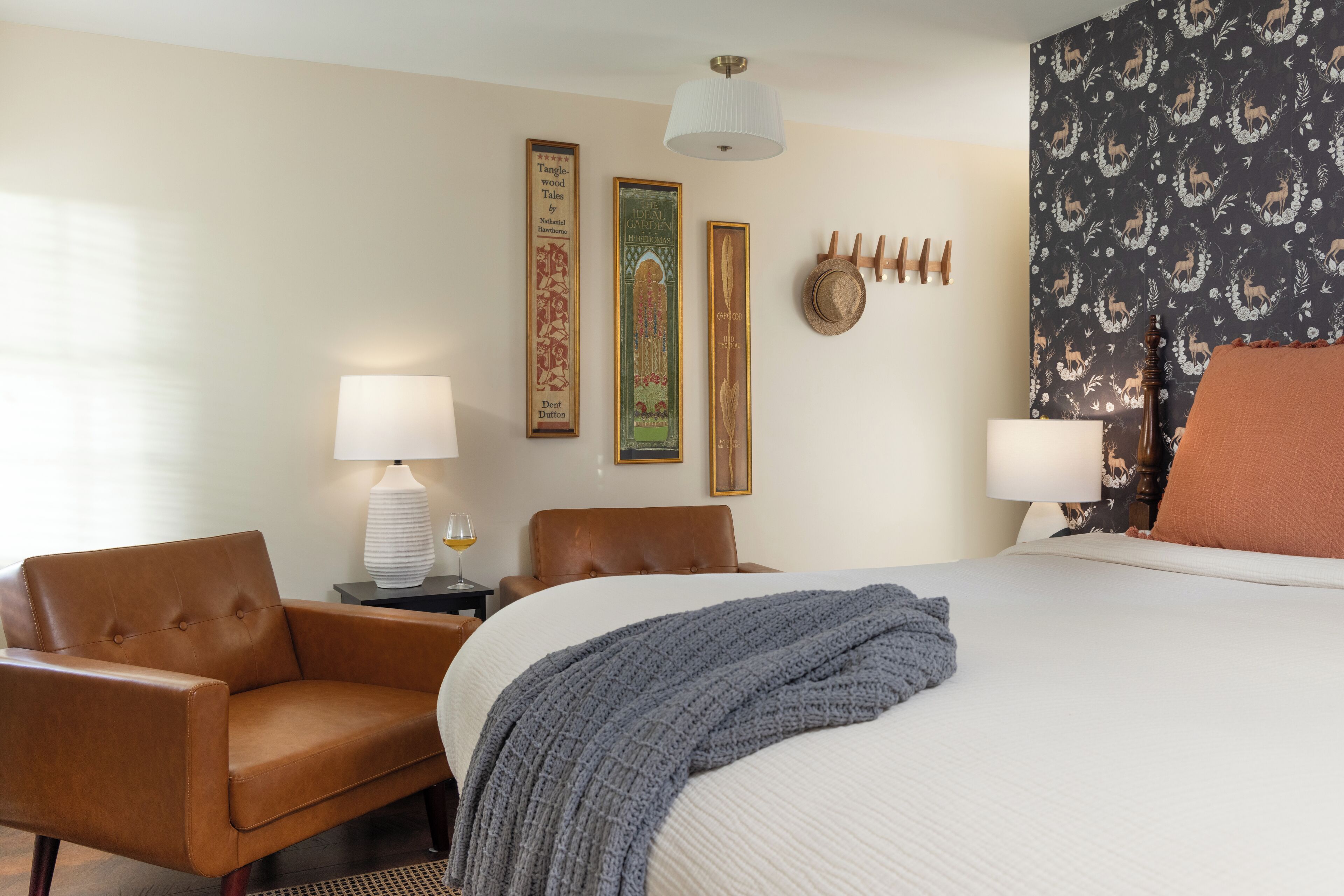 A hotel room with a bed, two chairs, a lamp, and decorative wall art.