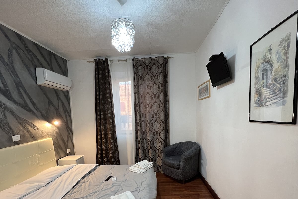 A hotel room with a bed, a chair, a TV, and a painting on the wall.