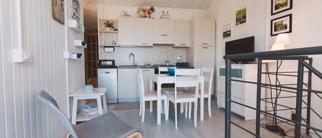 A compact kitchen with white cabinets, a dining area with a table and chairs, and a TV mounted on the wall.