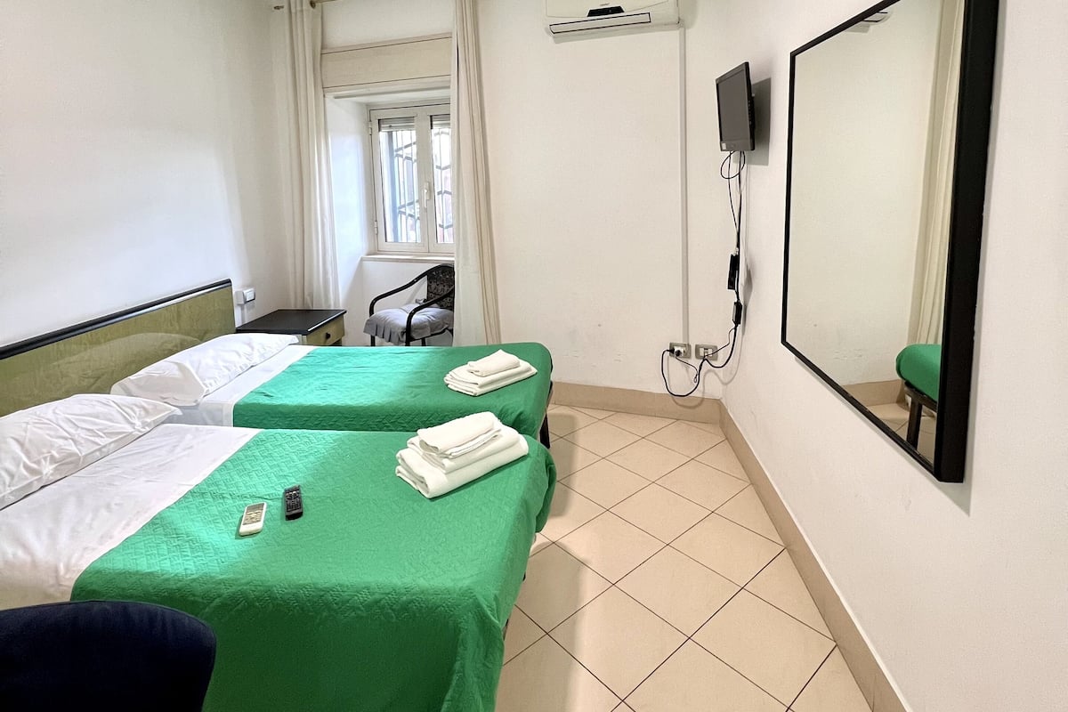 A hotel room with two beds, a desk, a chair, an air conditioning unit, a television, and a large mirror.