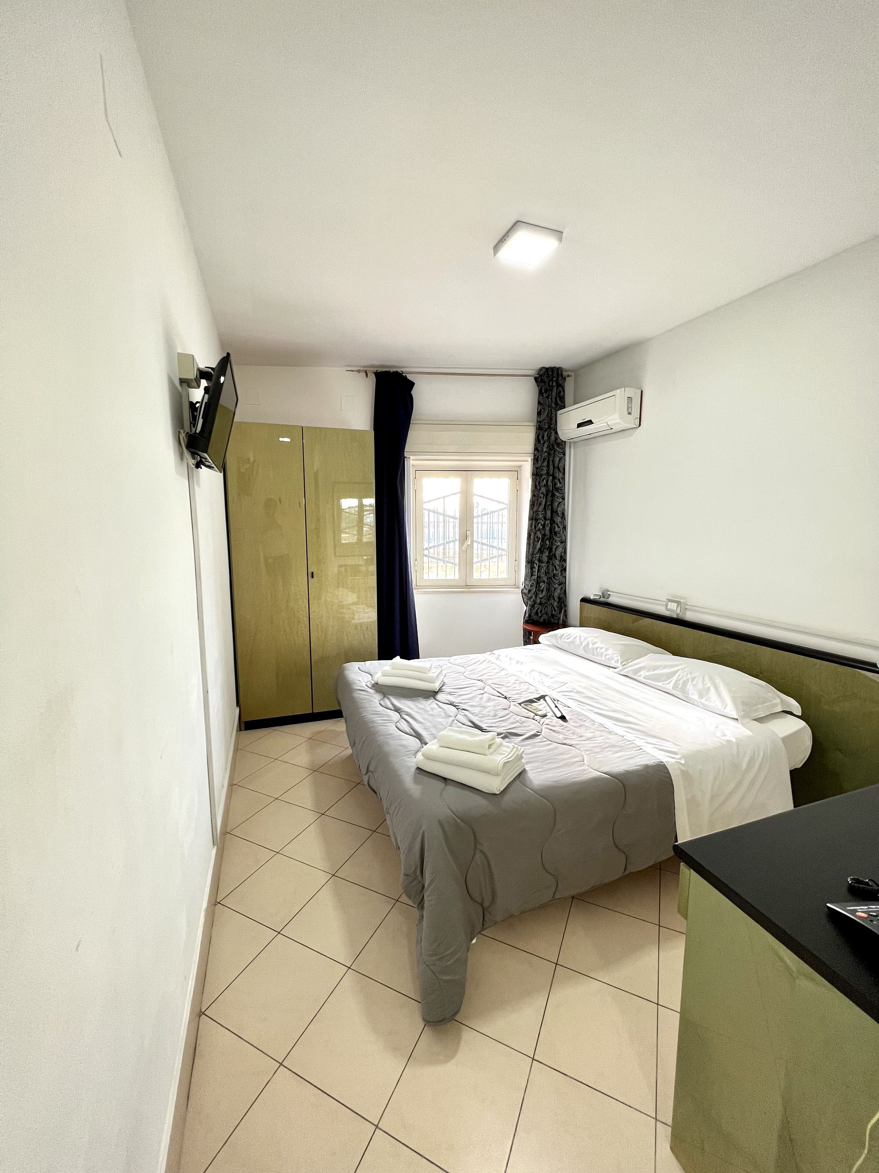 A bedroom with a bed, a desk, a wardrobe, and a window with curtains.