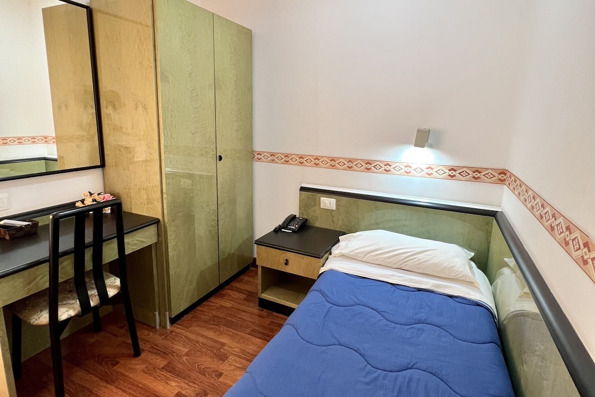 A small, neatly arranged bedroom with a single bed, a desk, a chair, and a wardrobe.