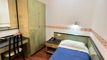 Un dormitorio pequeño y ordenado con una cama individual, un escritorio, una silla y un armario.
