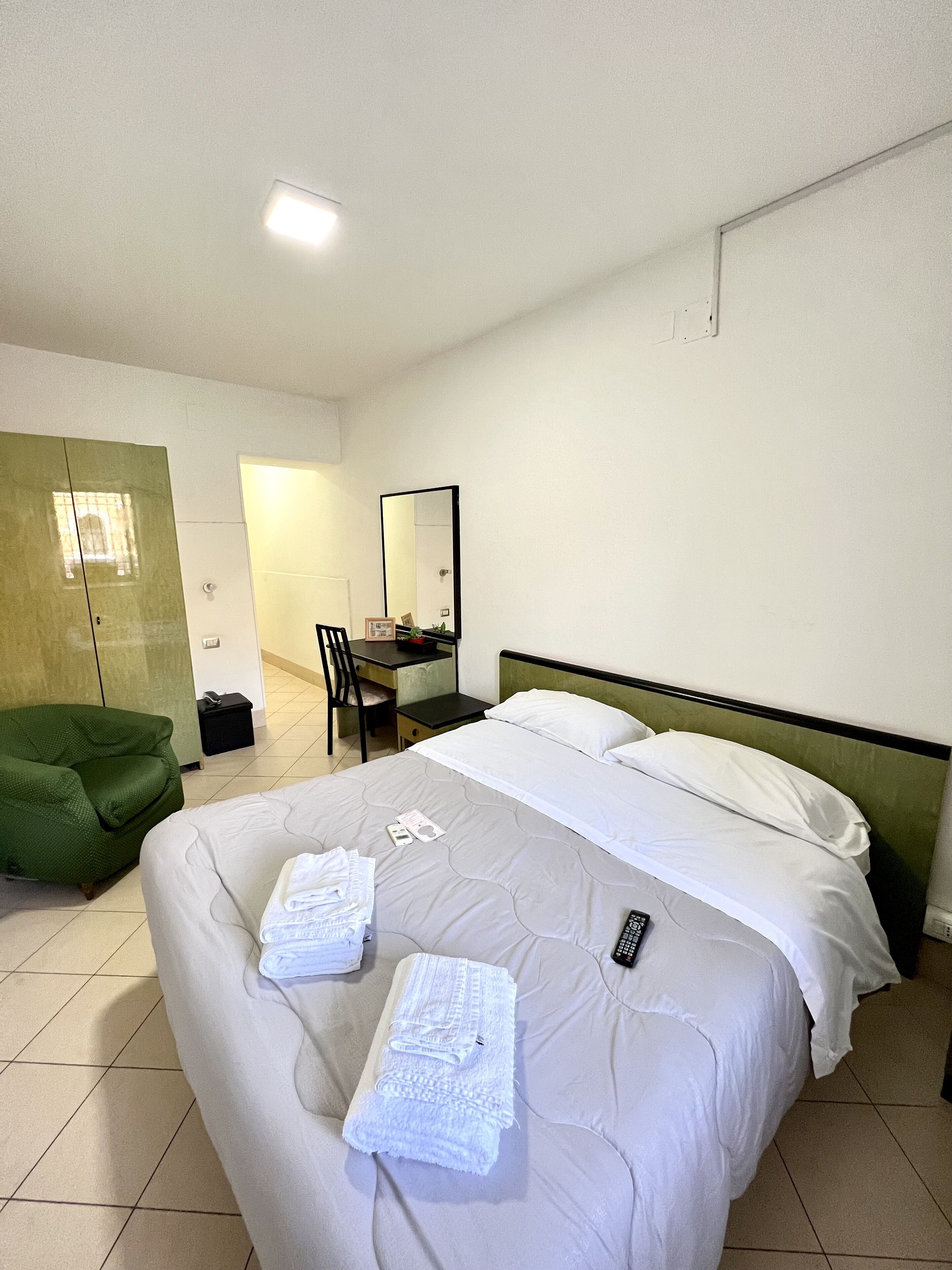 Een hotelkamer met een bed, een bureau, een stoel en een groene fauteuil.
