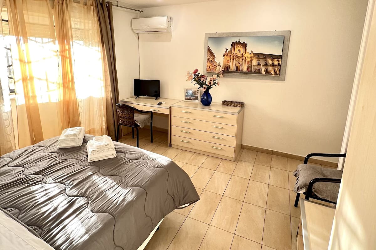 A bedroom with a bed, a desk, a chair, a dresser, and a painting on the wall.