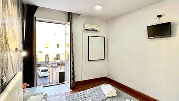 Habitación de hotel con cama, televisor de pantalla plana en la pared, aire acondicionado y vista al exterior a través de un vidrio.