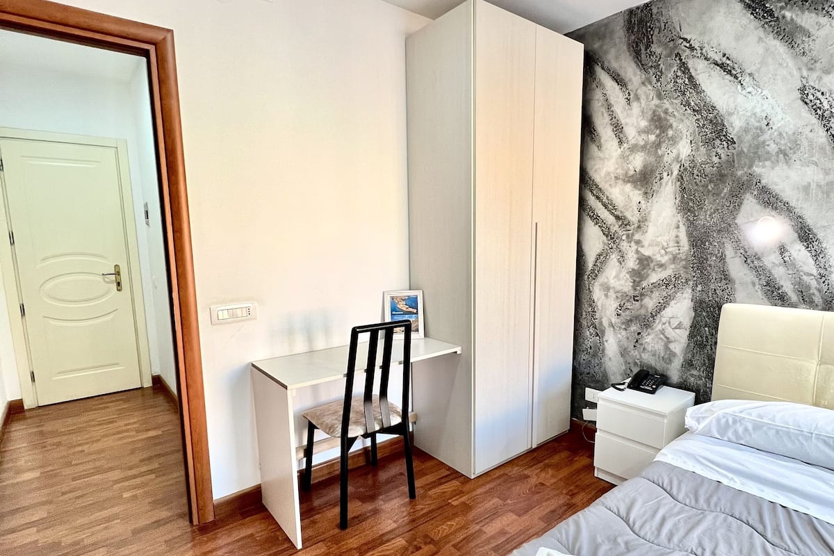 A bedroom with a bed, a desk, a chair, a wardrobe, and a wall with a textured design.