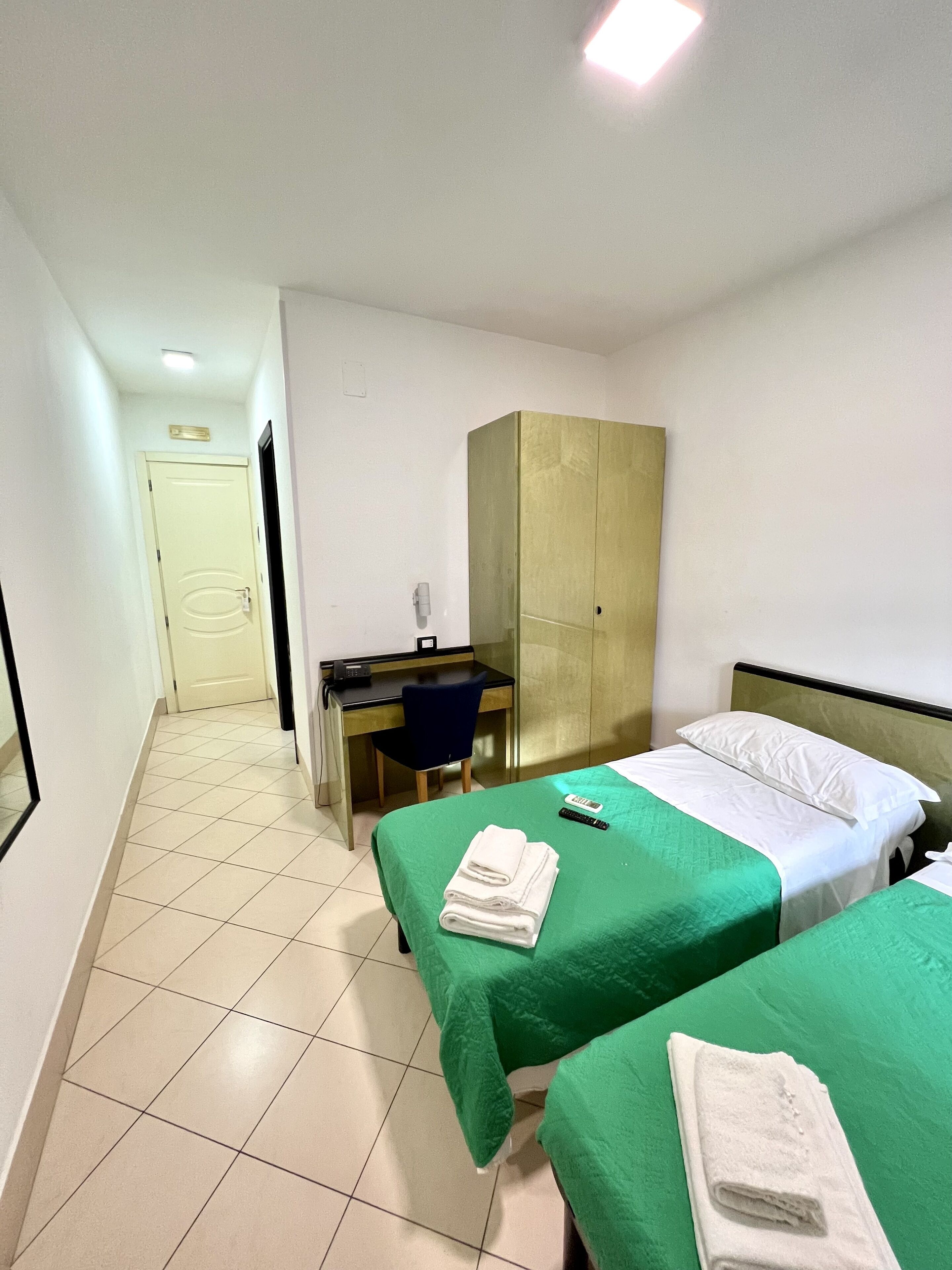 Quarto de hotel com duas camas, uma escrivaninha e um guarda-roupa.