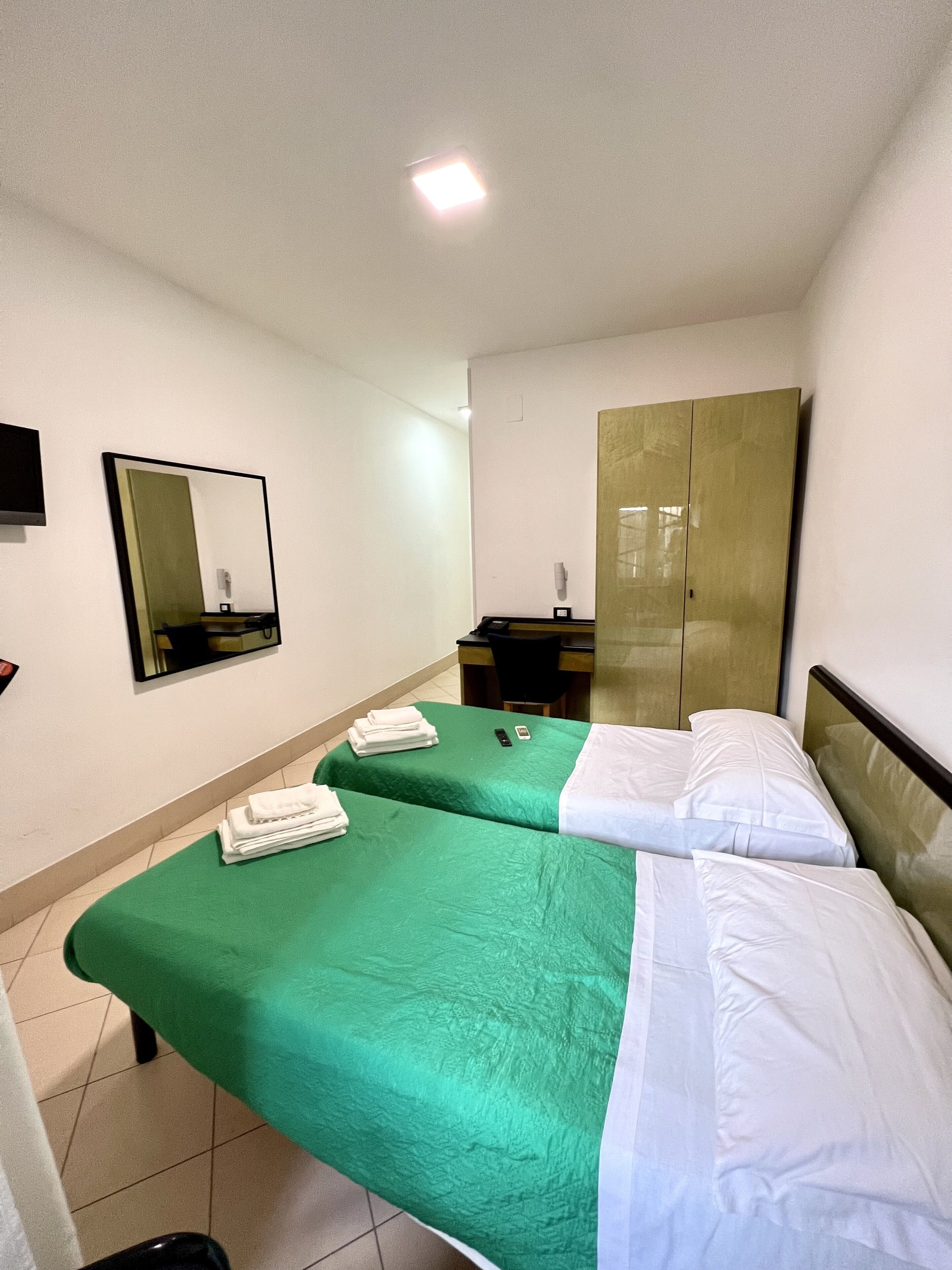 Habitación de hotel con dos camas, un armario, un escritorio, una silla, un espejo y una televisión.