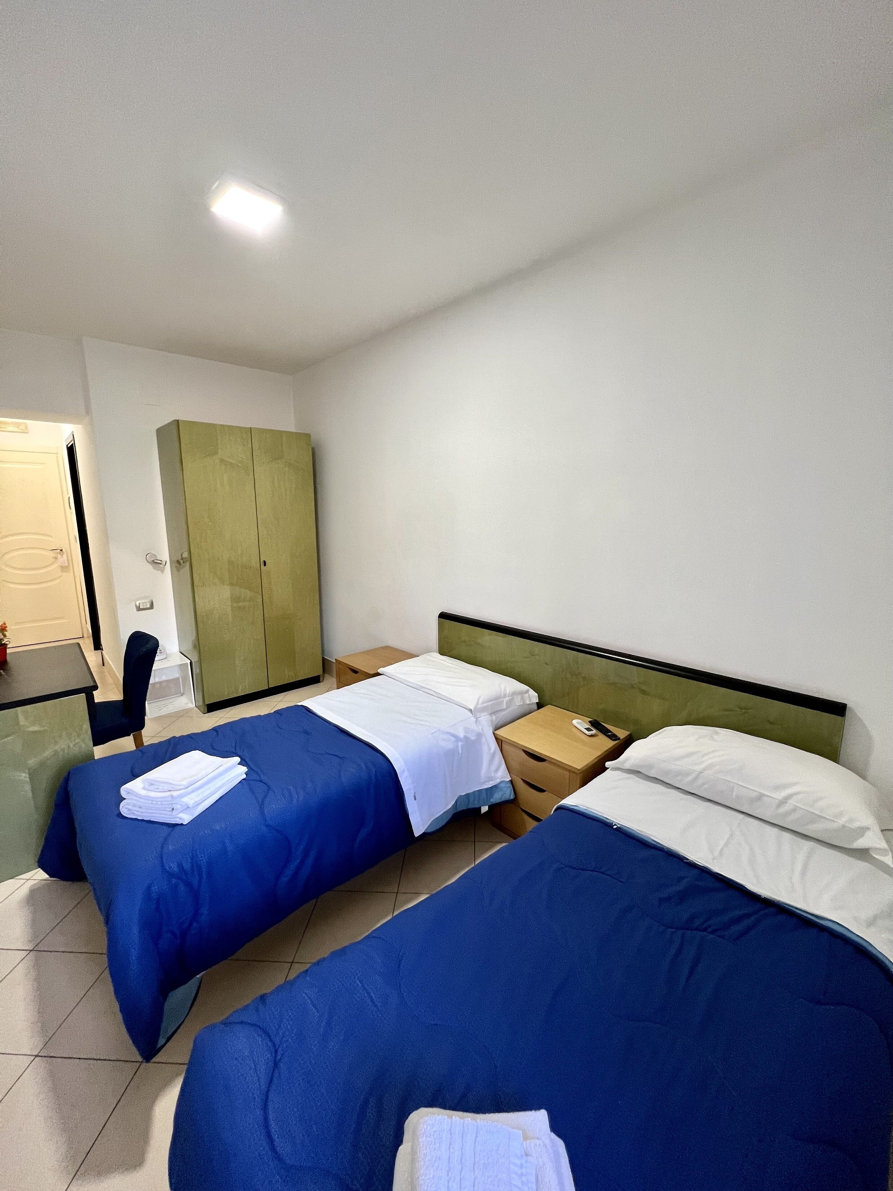 A hotel room with two single beds, a desk, a chair, and a wardrobe.