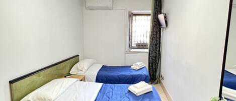 Una habitación pequeña y limpia con dos camas, un escritorio, una silla, un espejo y una ventana con cortinas.