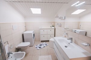 Ein modernes Badezimmer mit Waschmaschine, Toilette, Bidet und einem großen Waschbecken.