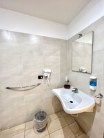 Un baño con un lavamanos blanco, un espejo, un perchero para toallas, un dispensador de jabón y un cubo de basura.