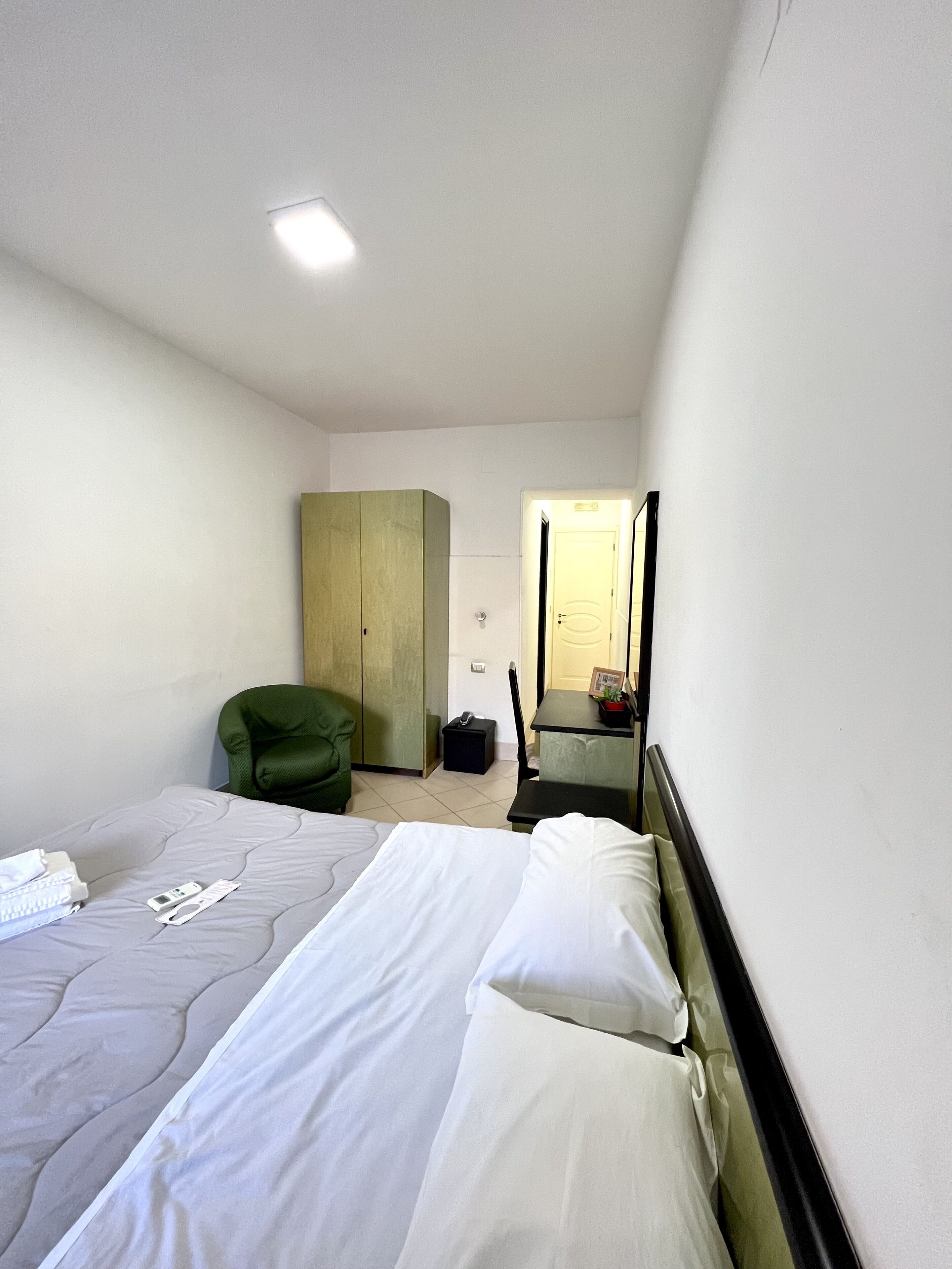 A small, clean room with a bed, a chair, a wardrobe, and a mirror.