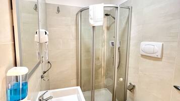 Une salle de bain moderne avec une douche à parois de verre, un lavabo blanc doté d’un distributeur de savon et des toilettes.