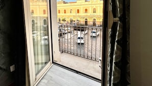 A room with a large window overlooking a street and a building with a clock tower. - Hotel Como (Syracuse)