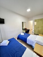 Habitación de hotel con dos camas, un escritorio, un espejo, un armario y un televisor.