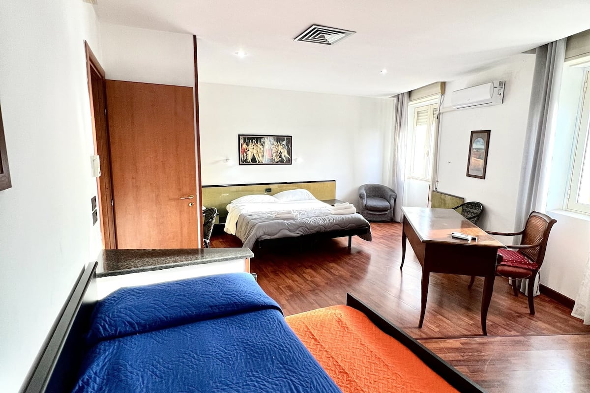 A hotel room with a bed, a desk, a chair, and a painting on the wall.