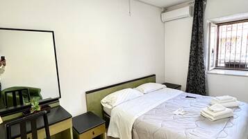 Un dormitorio con cama, escritorio, silla, espejo y ventana con cortinas.