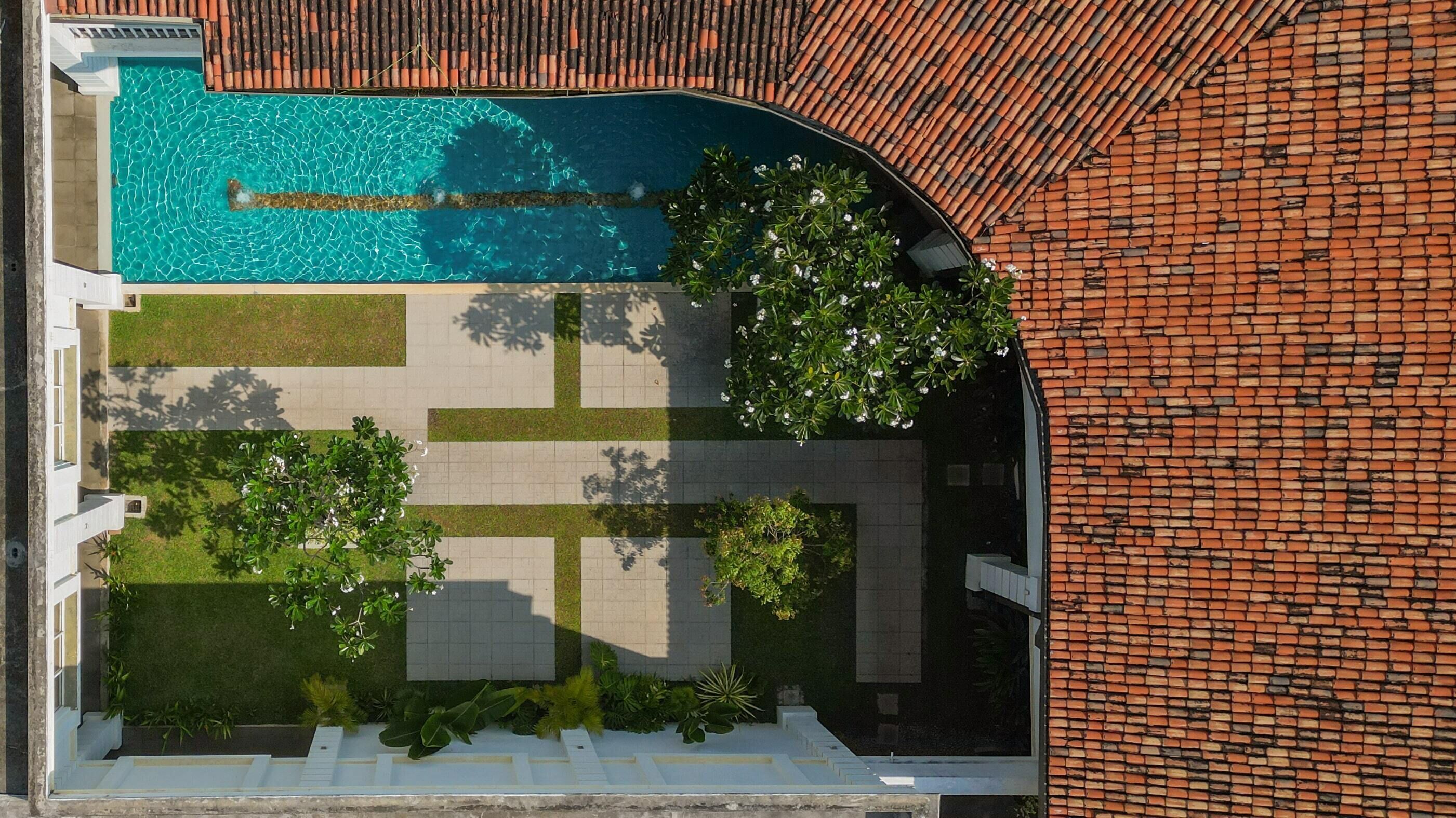 Vista aérea de una propiedad residencial con piscina, césped verde y pared de ladrillo.