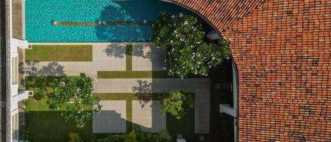 An aerial view of a residential property with a swimming pool, green lawns, and a brick wall.