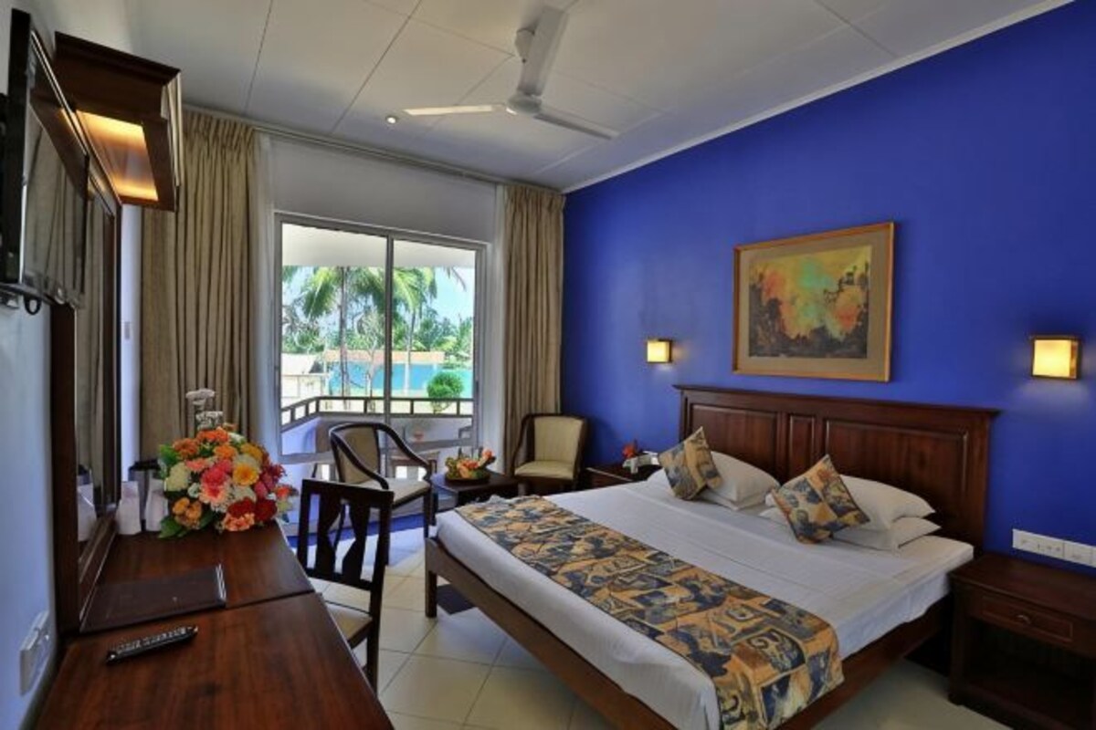 Ein Hotelzimmer mit Bett, Schreibtisch, Stuhl, einem Bild an der Wand und Blick ins Freie.