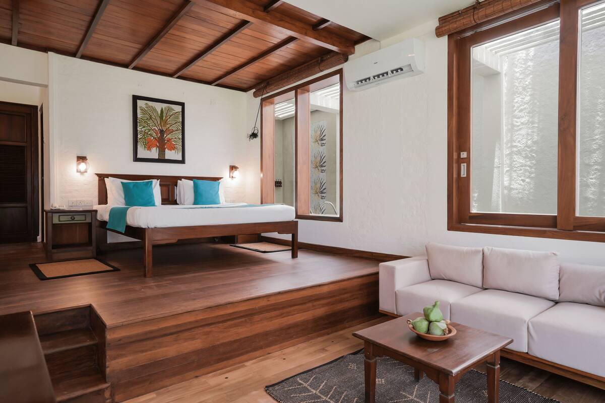 Ein Zimmer mit einem Bett, einer Couch, Holzboden, einem Fenster und einer Wand-Klimaanlage.
