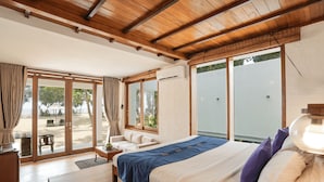 A bedroom with a bed, a nightstand, a lamp, and a view of the beach through large windows. - Hibiscus Beach Hotel And Villas (Wadduwa)