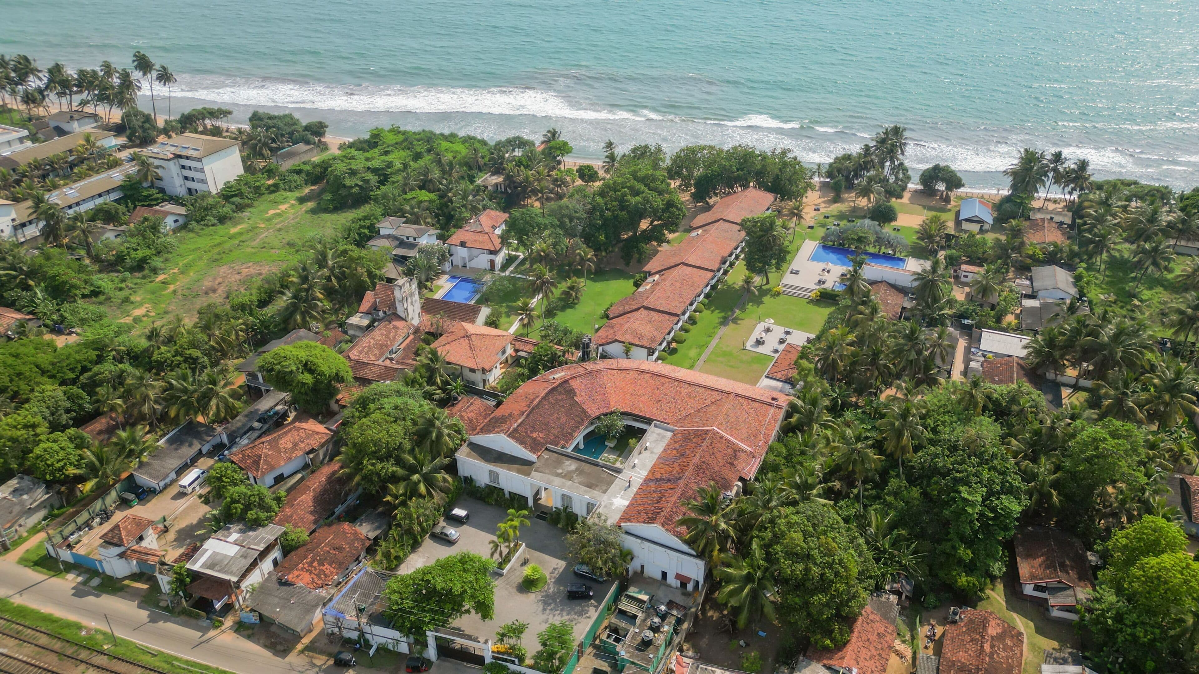 An aerial view of a coastal residential area with houses, a swimming pool, and a beach.