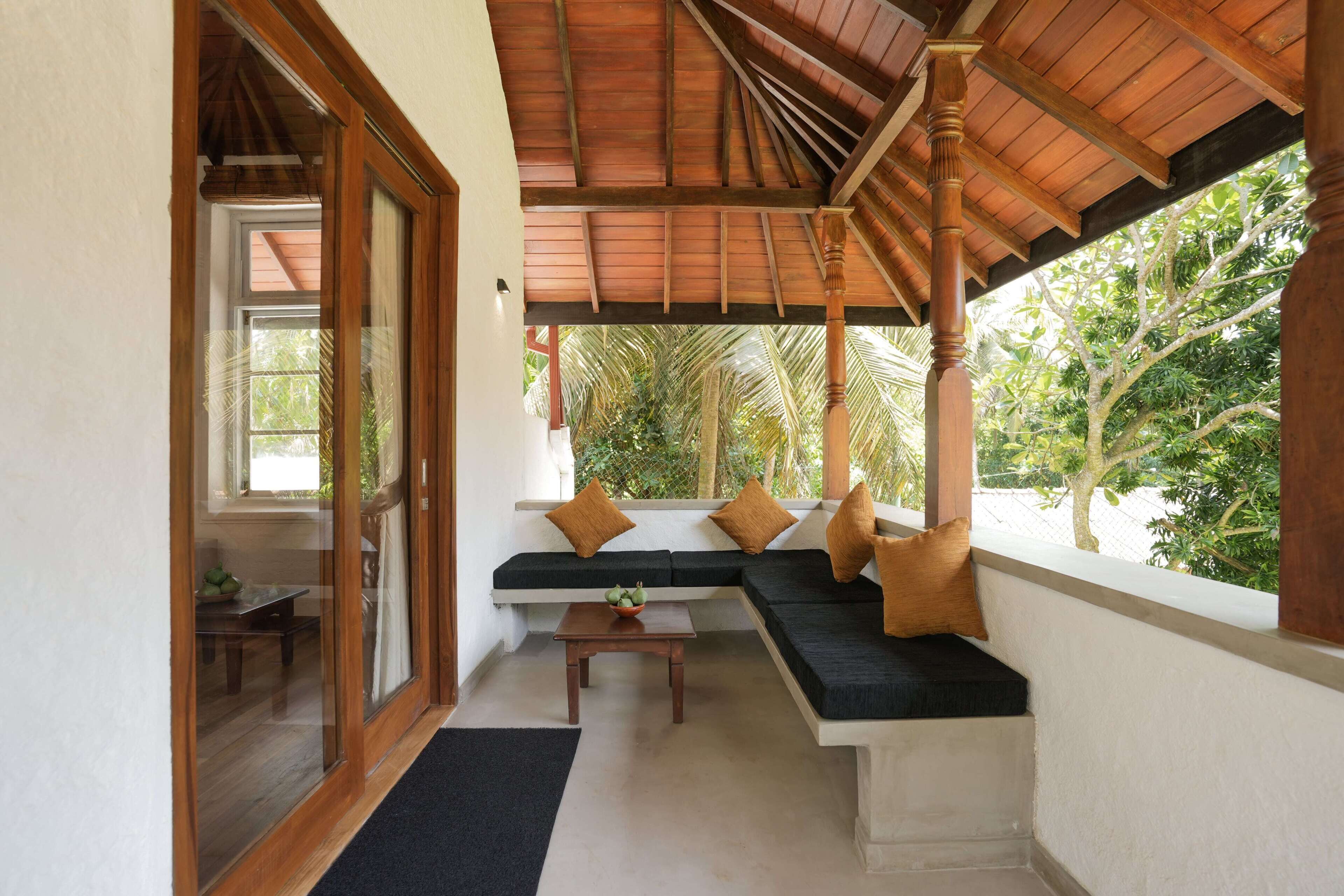 Una habitación con techo de madera, un sofá negro con cojines, una mesita y una ventana con vistas a la vegetación.
