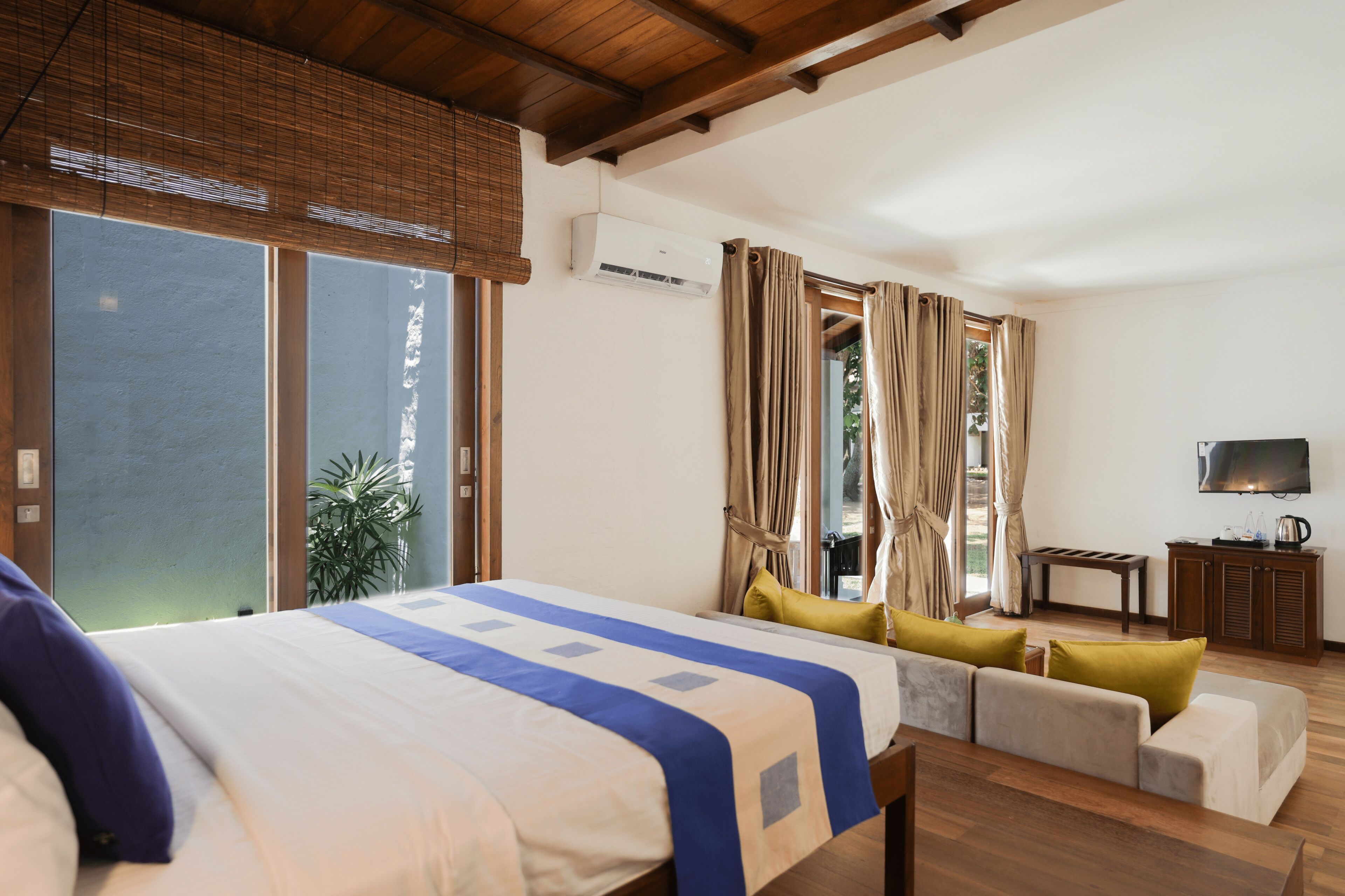 A hotel room with a bed, sofa, TV, and an air conditioning unit.