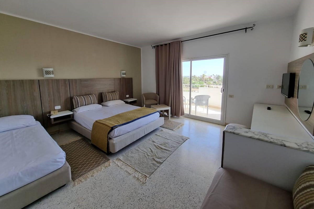 Une chambre d’hôtel équipée d’un lit, d’un bureau, d’une chaise, d’une télévision et d’un balcon avec vue.