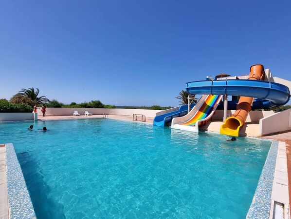 A swimming pool with a water slide, lounge chairs, and a clear blue sky. - Helya Beach Resort (Monastir)