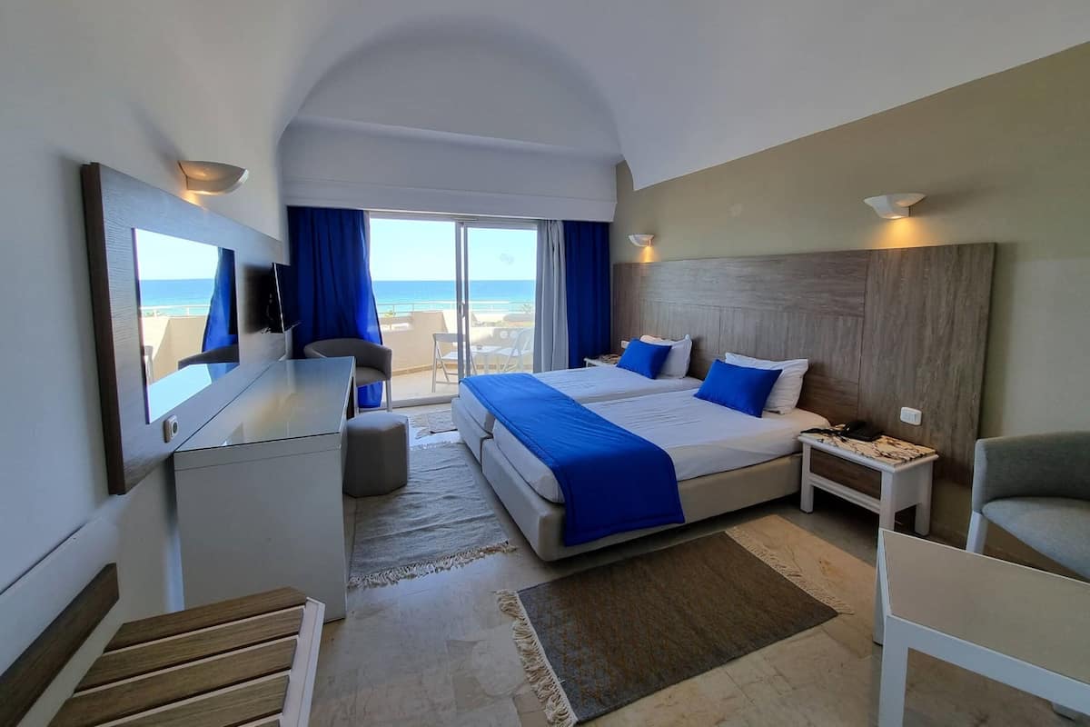Une chambre d’hôtel avec un grand lit, un bureau, une chaise et une télévision. Elle dispose d’un balcon avec vue sur l’océan.