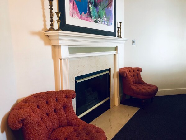 A room with a fireplace, two upholstered chairs, and a framed artwork above the mantel.