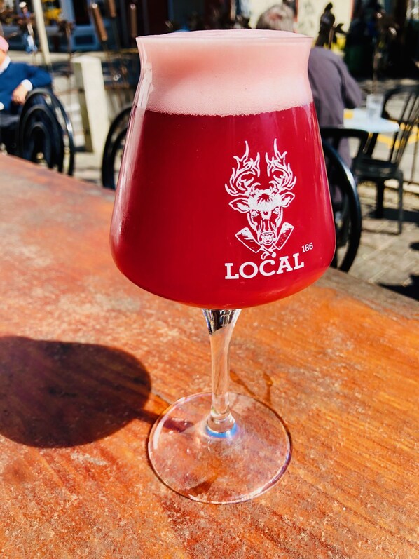 A glass of red beer with a logo and the word "LOCAL" on it, placed on a wooden table.