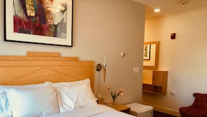 A hotel room with a large bed, a nightstand, a vase with flowers, a red chair, and a painting on the wall.