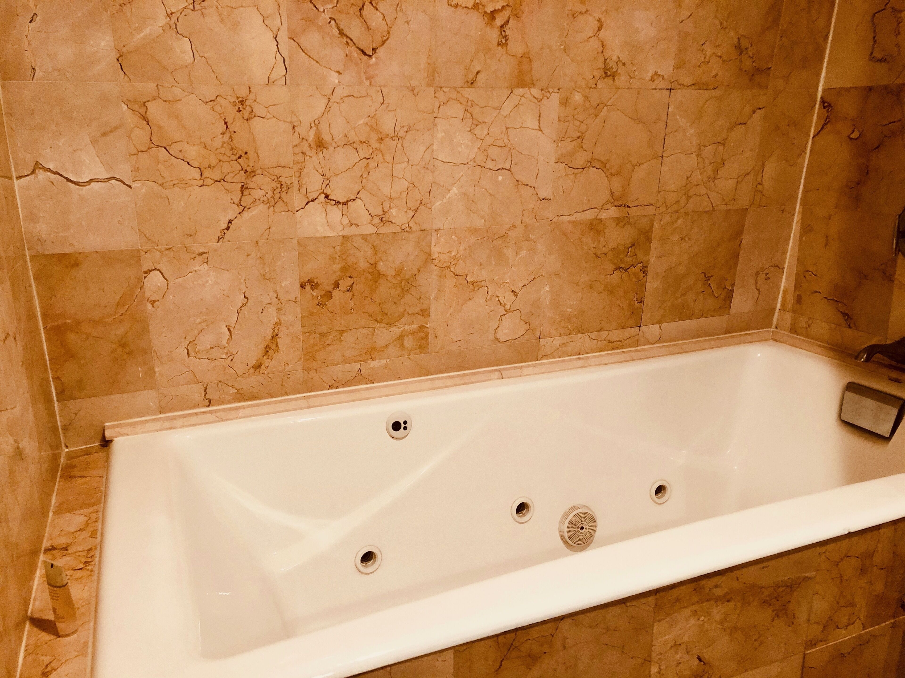 A bathroom with a rectangular bathtub, marble walls, and a white sink.