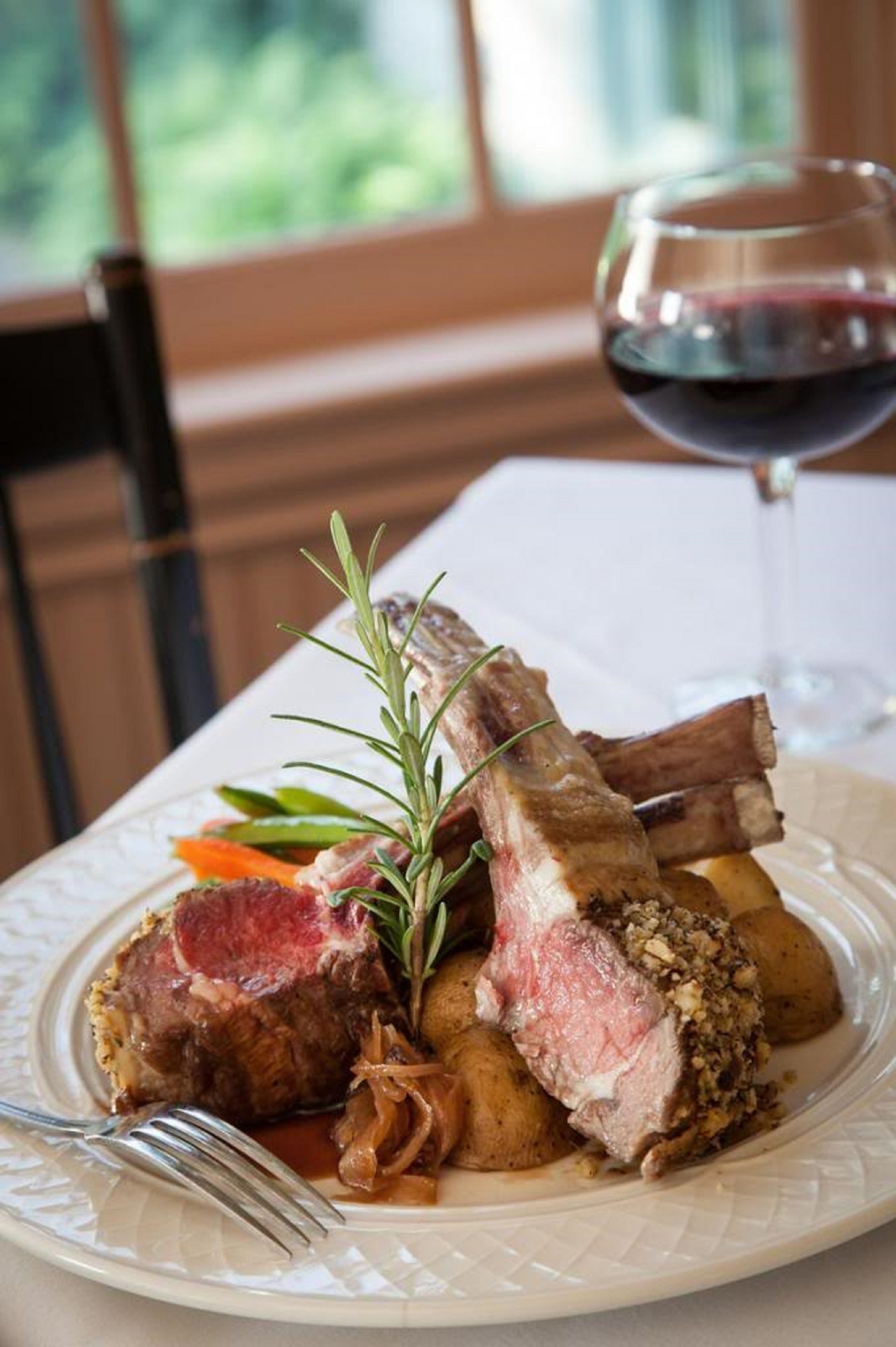 Un plato de comida con carne y verduras, una copa de vino tinto y un tenedor sobre una mesa.