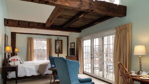A bedroom with a large bed, a blue armchair, a wooden desk, and a view through a glass door. - Chesterfield Inn (West Chesterfield)