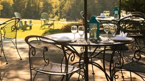 An outdoor dining area with tables and chairs, umbrellas, and a view of a forested landscape. - Chesterfield Inn (West Chesterfield)