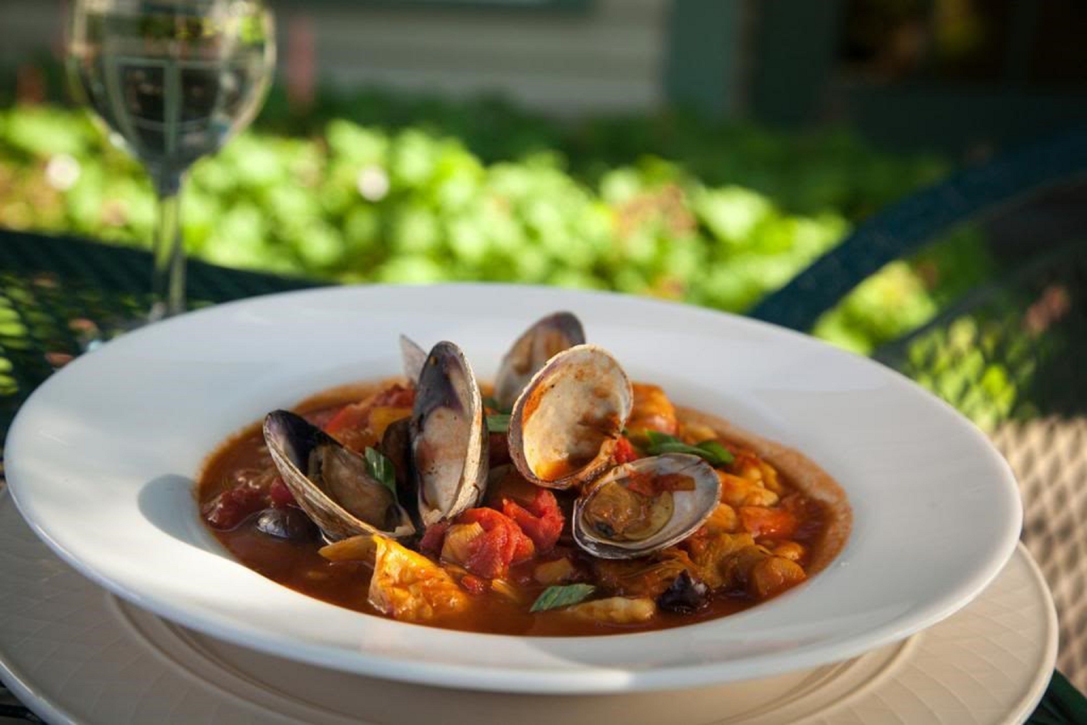 Un plato de estofado de mariscos con almejas, tomates y hierbas, servido en un plato blanco.