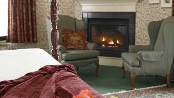 Ein Schlafzimmer mit einem Himmelbett, einem Kamin, zwei Sesseln und einem Teppich mit Blumenmuster.