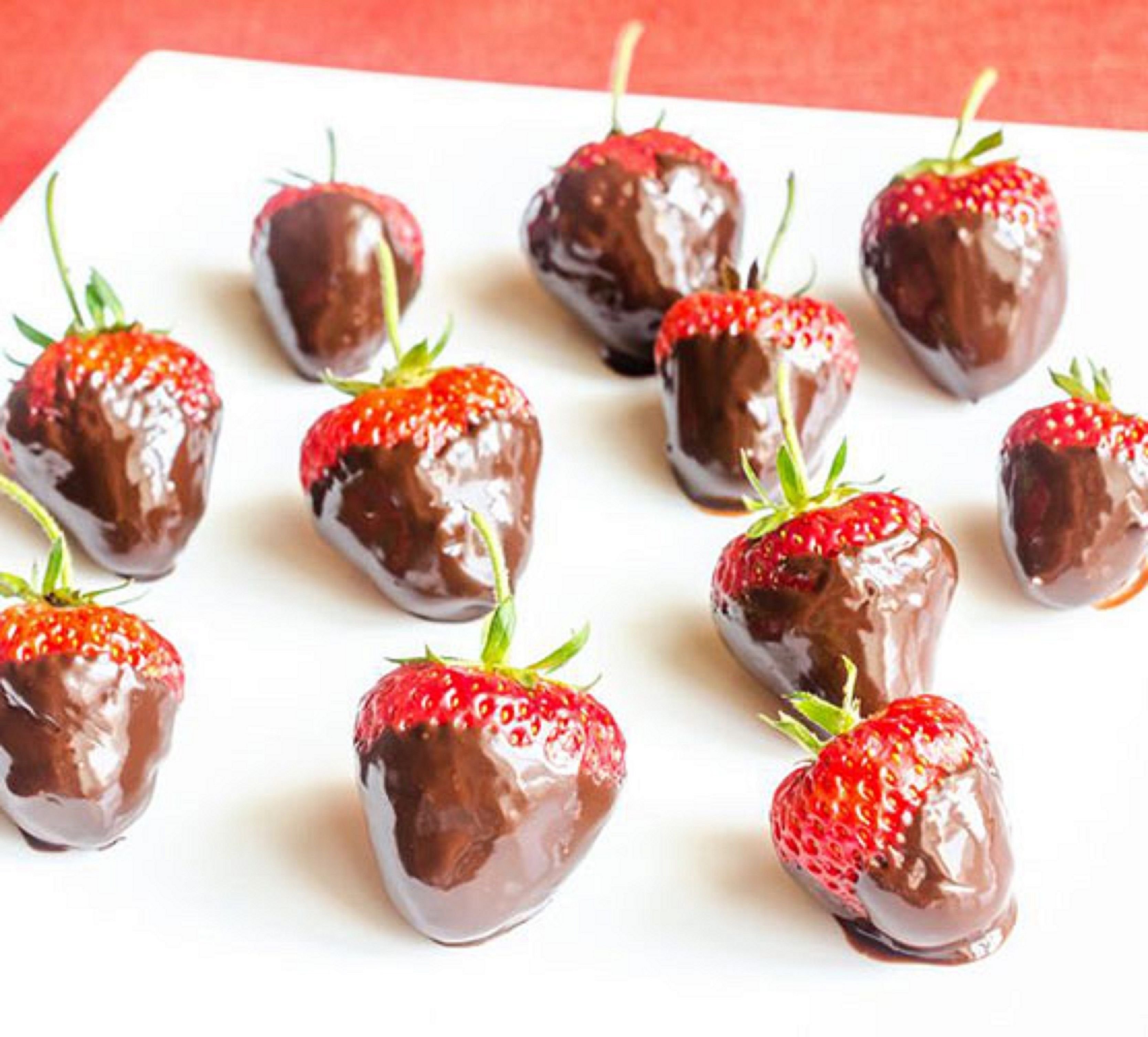 A white plate with chocolate-covered strawberries arranged on it.