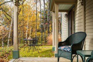 A covered porch with a table and chairs, surrounded by a forest with autumn foliage.